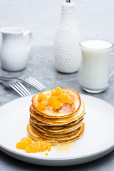 Delicious homemade pancakes with tangerines and honey, glass of milk on a plate on the table