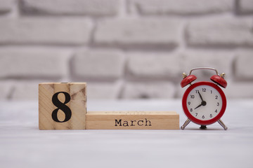 March 8. Day 8 of month on wooden calendar with red alarm clock on white brick background.