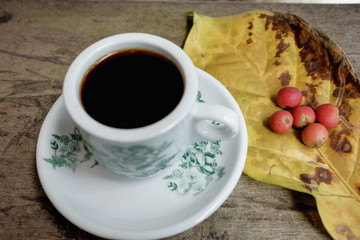 Hot coffee cup with fresh organic red coffee beans and the coffee leaf on the wooden table .