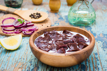 Pieces of raw beef liver soaked in milk in a wooden bowl and ingredients for cooking on the table