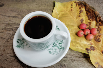 Hot coffee cup with fresh organic red coffee beans and the coffee leaf on the wooden table .