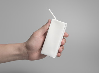 Carton of milk or juice package in hand on grey background for print design and mock up