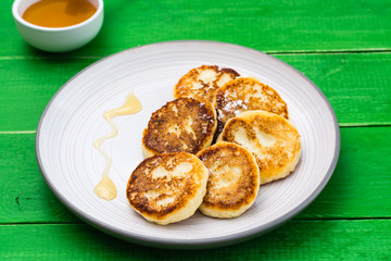 Homemade cottage cheese pancakes with honey on a plate on a wooden table