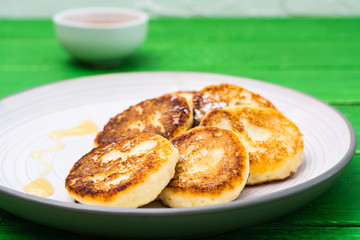 Close-up of homemade cottage cheese pancakes with honey on a plate on a wooden table