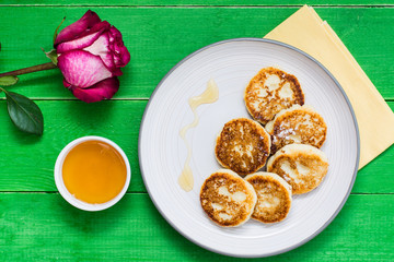 Homemade cottage cheese pancakes with honey and rose on a plate on a wooden table. Top view