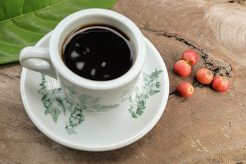 Hot coffee cup with fresh organic red coffee beans and the coffee leaf on the wooden table .