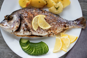 Baked dorada with potatoes on a white plate.