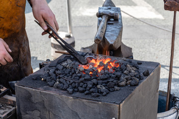 A blacksmith heating the metal stirrup hook he is making in a red hot glowing blacksmiths fire ...