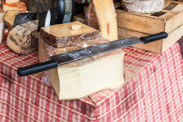 Whole French cheese with large two handed slicing knife on top.  On a red and white check cloth