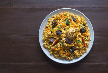 Uzbek pilaf in a plate on a brown wooden table. 