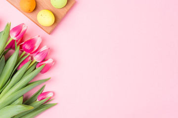 Easter holiday background with small with colored eggs and pink flowers tulip. Flat lay. Copy space. Space for text.