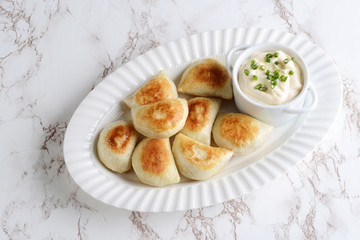 top view pierogies on a white platter with sour cream and spring onions