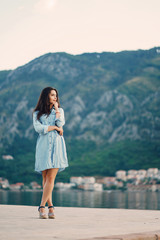 A beautiful young girl in a blue dress standing near water