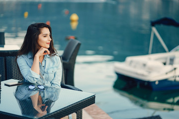 A beautiful young girl in a blue dress sitting near water and use the phone