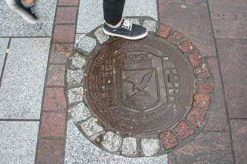 A sewage hatch is on a municipal area. Wet sewage hatch and leg of man.