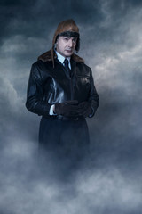 Vintage pilot in cap under stormy sky.