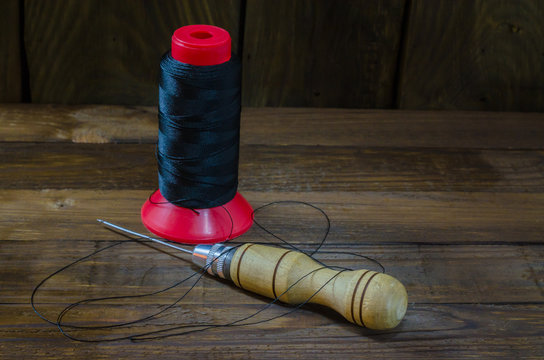Shoe awl next to nylon thread on a wooden background.