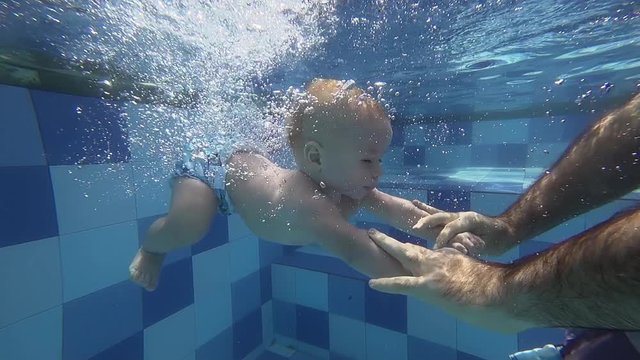 Happy smiling toddler is diving under water with father