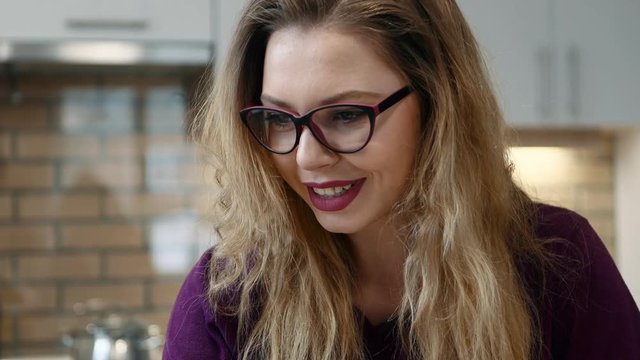 Woman learns on a computer and and writes notes in notepad in the kitchen at home.
