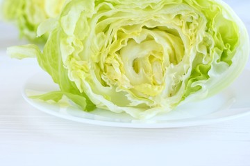 Half of fresh green lettuce salad on a white plate. Healthy vegetable food. Juicy iceberg salad for vegetarian or dietary snack. Delicious organic green salad with selective focus