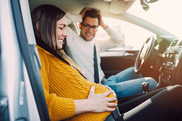 Pregnant woman starting to feel pain and contractions while her worried husband driving a car. She...