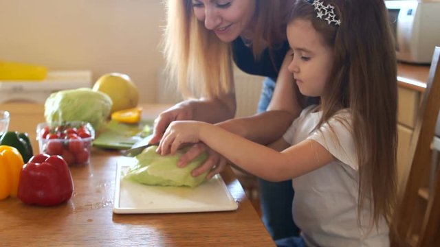 Mom and little daughter in the kitchen cut cabbage for a vegetarian salad. Mom's helper