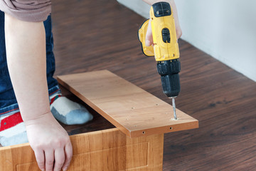 is the process of assembling furniture from chipboard. in the hands of a rechargeable screwdriver for tightening screws.