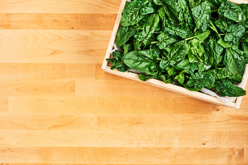 Fresh spinach leaves with water drops in wooden box on wooden table. Top view with copy space for text.