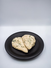 Healthy chicken breasts with herbs put in black plate on white background.