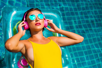 Amazing beautiful girl in a yellow bikini air mattress swims in the pool of a luxury hotel, summer vacation, happiness, travel, smile joy, listening to music, drinking cocktail - obrazy, fototapety, plakaty