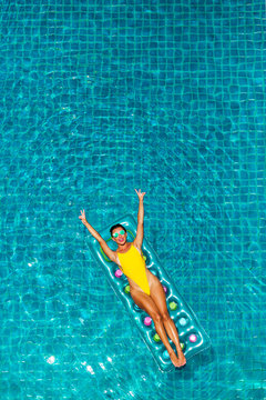 Gorgeous beautiful lady in sexy yellow bikini swims in a luxury hotel pool on an inflatable mattress. Summer holidays, travel, all inclusive. Top view on quadcopter