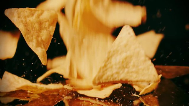 Slow motion shot of crispy tortilla chips falling on the tale against black background, close-up shot