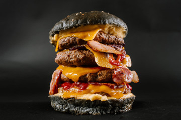 A very big black burger with three cutlets on the black background