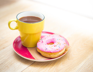 The donut with pink icing and the yellow cup of coffee are in a flat plate