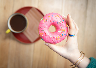 The donut with pink icing in the hand of the girl and coffee on the table