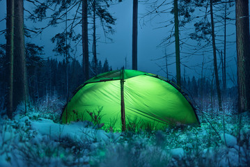 Glowing green tent in the night winter forest