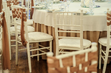 close up photo of white chairs decorated with brown textil in a banquet hall in white and brown colors decorated for the event
