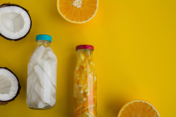 Detox water with coconut and orange in the glass bottles on the yellow  background.Top view.Copy space.