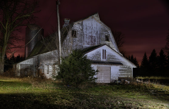 Low key old white barn at night. Silo, pine trees in background. Colorful sunset sky of red and purple. Long exposure light painting.