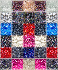 Multi-colour patchwork pattern of glass crystal beads in compartment box for crafting own jewelry, close up, top down view. 