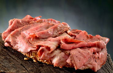 Roast beef open sandwich.  Rare roast beef, thinly sliced on thick slice of whole grain bread and lightly seasoned with black pepper.  - obrazy, fototapety, plakaty