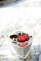 Chia pudding with strawberries and chocolate on white marble surface