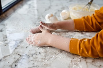 Fototapeta premium Child's hands mixing ingredients, some flour and eggs on white marble surface near the window 