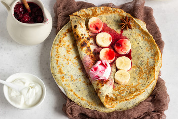 Vanilla poppy seed pancakes or crepes with natural yogurt, banana and cherry sauce with spices (cinnamon and anise). Light concrete background. Copy space.