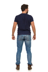 Man In Jeans And Blue T-shirt Is Standing Legs Apart And Looking Away. Rear View.