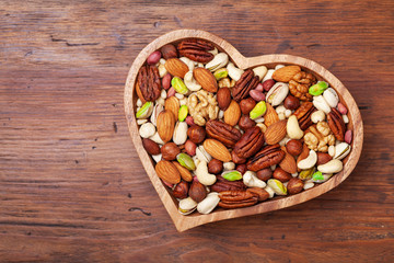 Heart shaped bowl with mixed nuts on wooden table top view. Healthy food and snack.