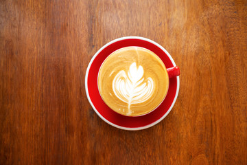 Cup of hot coffee with latte art in leaf shape. Favorite beverage for freshness and caffeine. Top view with copy space on wooden table.