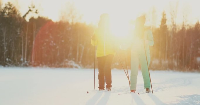 In the winter forest at sunset a man and a woman ski and look around at the beauty of nature and attractions in slow motion.