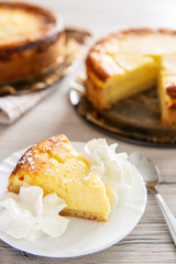 Ein Stück Käsekuchen oder Quarkkuchen auf weißem Teller dahinter ganzer und angeschnittener...