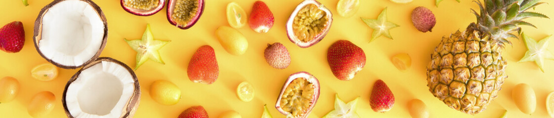 Backdrop or banner of exotic tropical fruits background. Colorful fresh exotic fruits on yellow desk. Pineapple, coconut, passion fruit, strawberry, carambola. Flat lay, top view, copy space